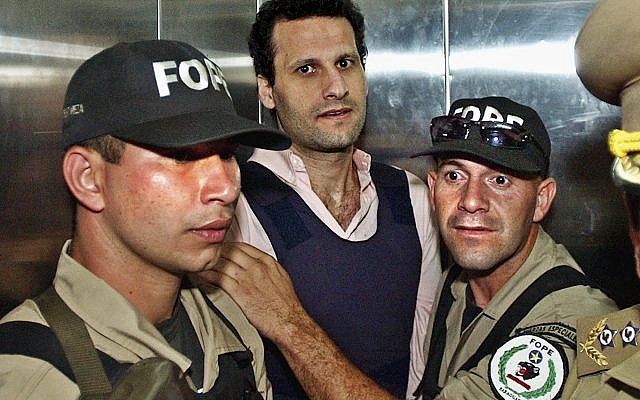 In this Nov. 17, 2003 file photo, Lebanese citizen Assad Ahmad Barakat, who was then facing tax evasion charges, is escorted by police to a courthouse in Asuncion, Paraguay. On Friday, Sept. 21, 2018, federal police in Brazil arrested Barakat, a fugitive accused of belonging to Lebanon's Hezbollah militia and of being a key financier of terrorism.  (AP Photo/Jorge Saenz)