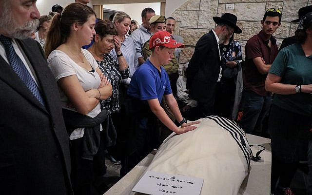 The son of Ari Fuld places his hands on his father's body at his funeral in Kfar Etzion on September 17, 2018. (Gershon Elinson/FLASH90)