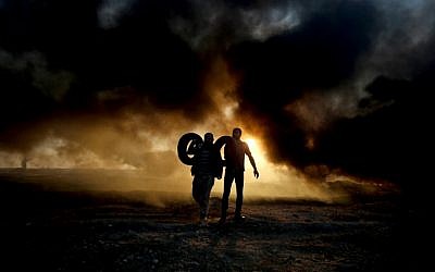 Palestinian protesters carry tires as smoke billows from burning tires at the Israel-Gaza border, east of Gaza city, on October 12, 2018 (Photo by SAID KHATIB / AFP)