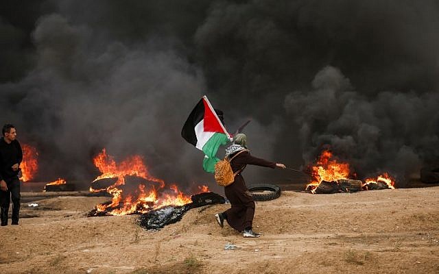 A Palestinian woman runs with a Palestinian flag, amid black smoke from tires burned by protesters, during clashes following a riot near the border with Israel east of Gaza City on October 26, 2018. (Photo by MAHMUD HAMS / AFP)