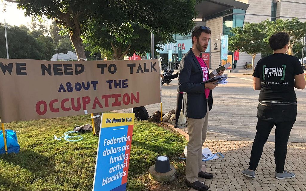 All That’s Left activists hand out fliers in front of a banner reading, ‘We need to talk about the occupation,’ at the Jewish Federations of North America General Assembly in Tel Aviv, Wednesday, October 24, 2018. (Steven Davidson/ Times of Israel)
