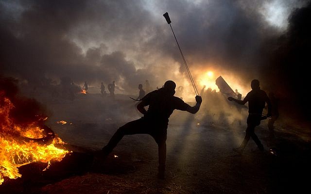 Black smoke from burning tires covers the sky as Palestinian protesters hurl stones toward Israeli troops during a protest at the Gaza Strip's border with Israel, Oct. 12, 2018. (AP Photo/Khalil Hamra)