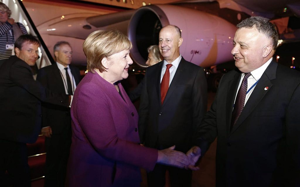 Illustrative: German Chancellor Angela Merkel shakes hands with Israeli Ambassador to Germany Jeremy Issacharoff at Ben Gurion Airport on October 3, 2018, as Minister Tzachi Hanegbi looks on. (Avi Davidi/Foreign Ministry)