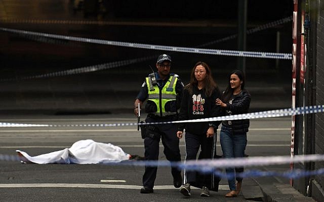 A police officer directs people away from the crime scene as a body is seen covered with a white sheet in Melbourne on November 9, 2018 (Photo by WILLIAM WEST / AFP)