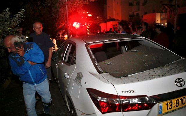 Two men walk past a vehicle that was hit by a rocket fired from the Gaza Strip, in the southern Israeli town of Ashkelon, on November 12, 2018. (GIL COHEN-MAGEN / AFP)
