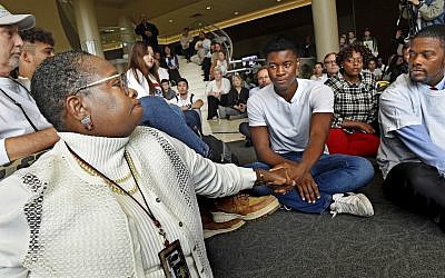 Aura Wharton-Beck, left, an assistant professor in the School of Education at the University of St. Thomas and a graduate of the school, clasps hands with Kevyn Perkins, center, during a moment of silence before a protest in the Anderson Student Center at the University of St. Thomas in St. Paul, Minnesota, October 25, 2018. (Jean Pieri/ Pioneer Press via AP)