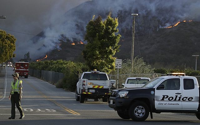 A police officer mans a checkpoint in front of an advancing wildfire Thursday, Nov. 8, 2018, near Newbury Park, Calif. The Ventura County Fire Department has also ordered evacuation of some communities in the path of the fire, which erupted a few miles from the site of Wednesday night's deadly mass shooting at a Thousand Oaks bar. (AP Photo/Marcio Jose Sanchez)