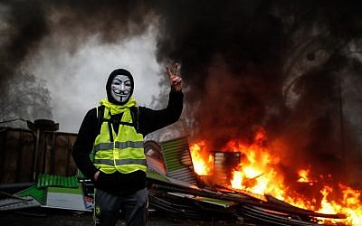 A protester wearing a Guy Fawkes mask makes the 'Victory' sign during a protest of the Yellow Vests against rising oil prices and living costs, on December 1, 2018, in Paris. (AFP/Abdulmonam Eassa)
