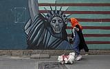 A woman walks her dog past a satirical drawing of Statue of Liberty on the wall of the former US Embassy in Tehran, Iran, May. 8, 2018. (Vahid Salemi/AP)