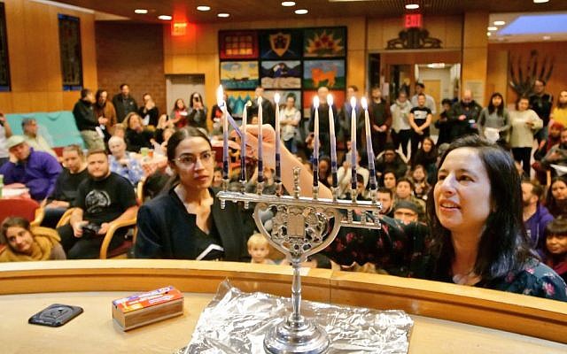 Alexandria Ocasio-Cortez (L) helps light a candle at a Hannukah celebration on December 9, 2018 ( Jews for Racial & Economic Justice/Twitter)