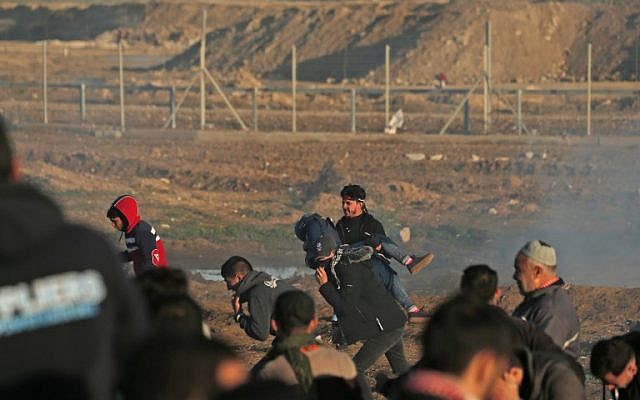 A Palestinian carries an injured youth as he runs with others from tear gas fumes during clashes with Israeli forces during a demonstration along the border with Israel east of Gaza City on January 11, 2019. (Mahmud Hams/AFP)