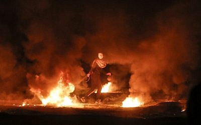 A masked Palestinian pulls a burning tire during a night demonstration near the fence along the border with Israel, east of Gaza City, on February 11, 2019. (Mahmud Hams/AFP)