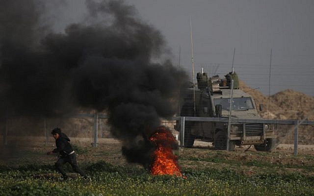 A Palestinian protester runs near burning tires during a demonstration near the fence along the border with Israel, east of Gaza City, on February 15, 2019. An Israeli military vehicle is pictured on the other side of the fence. (Said Khatib/AFP)