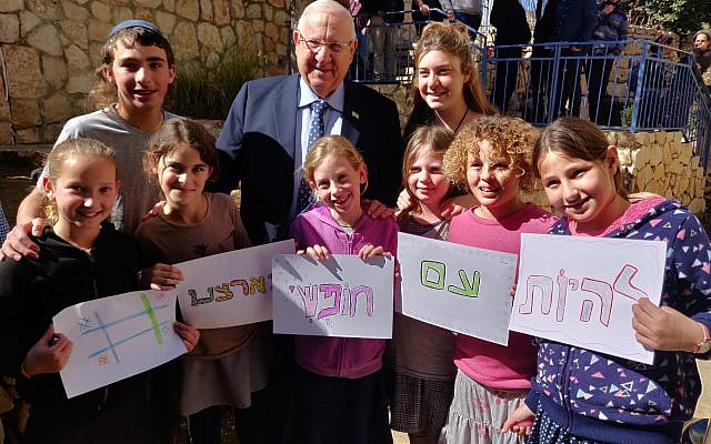 President Reuven Rivlin (c) stands with a group of children holding signs that read "to be a free people on our land," after paying a condolence visit at the home of Ori Ansbacher's family in the Tekoa settlement on February 13, 2019. (Courtesy)