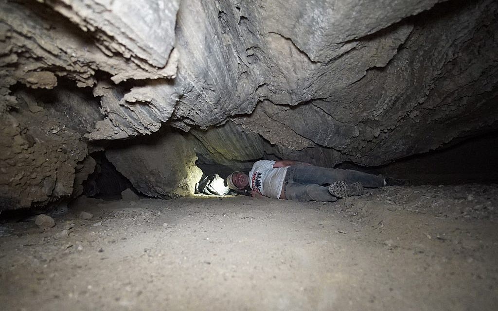 A researcher squeezes through a narrow opening in the Malcham Cave on March 22, 2019, near the Dead Sea. (courtesy Anton Chikishev/Hebrew Unviersity)