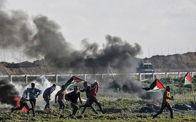 Palestinians holding Palestinian flags walk past burning tires during clashes near the security fence along the border with Israel, east of Gaza City, on February 22, 2019. (Mahmud Hams/AFP)
