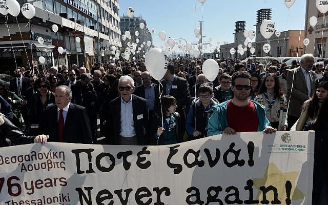 People hold a banner and balloons reading 'Never Again' as they walk toward the old railway station to mark the departure of the first train from Thessaloniki to the Auschwitz concentration camp in Poland on March 15, 1943, during a silent march in memory of Holocaust victims in Thessaloniki, on March 17, 2019. (Sakis MITROLIDIS / AFP)