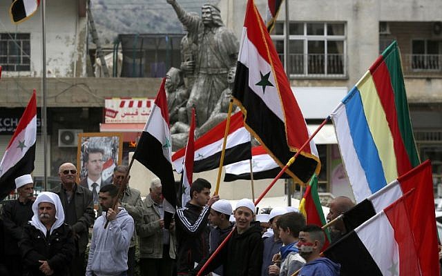 Residents of the Golan Heights wave Syrian and Druze flags as they gather in front of a portrait of Syrian President Bashar Assad during a protest against US President Donald Trump's recognition of Israeli sovereignty over the contested area, in the town of Majdal Shams, on March 23, 2019. (Jalaa Marey/AFP)