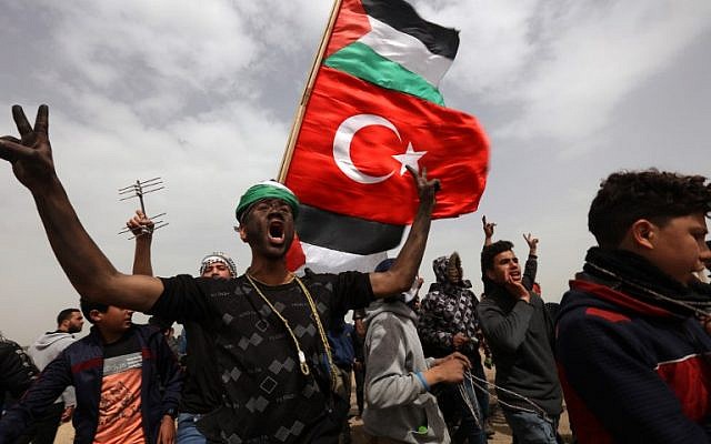 A Palestinian protester with black face-paint flashes the victory sign while marching with others flying Palestinian and Turkish national flags, during a demonstration marking the first anniversary of the "March of Return" protests, near the border with Israel east of Gaza City on March 30, 2019. (ANAS BABA / AFP)