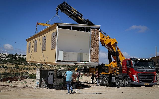 A crane lowers a caravan to the ground in a new settlement meant to resettle the evacuees of Netiv Ha'avot, in Gush Etzion, in the West Bank, May 9, 2018. (Gershon Elinson/Flash90)