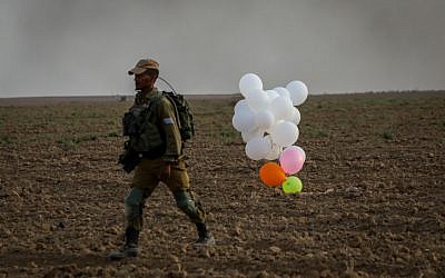 Illustrative. An Israeli soldier stands near balloons released by Palestinian protesters from the Gaza Strip that landed inside Israel on October 19, 2018. (Yossi Zamir/Flash90)