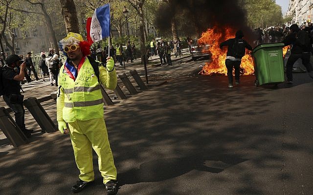 A protester waves a French flag as a dumpster burns in the background during a yellow vest demonstration in Paris, April 20, 2019. (AP Photo/Francisco Seco)