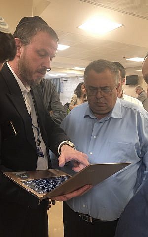 Likud strongman David Bitan (in blue shirt) huddles over a lap top computer with an activist from United Torah Judaism outside the Central Elections Committee. April 11, 2019. (Sue Surkes/Times of Israel)