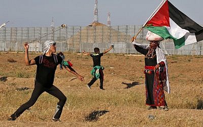 A protester hurls stones at Israeli troops as a woman wearing a traditional Palestinian outfit waves a national flag, during a demonstration near the border with Israel, east of Gaza City, on May 10, 2019. (Said KHATIB / AFP)