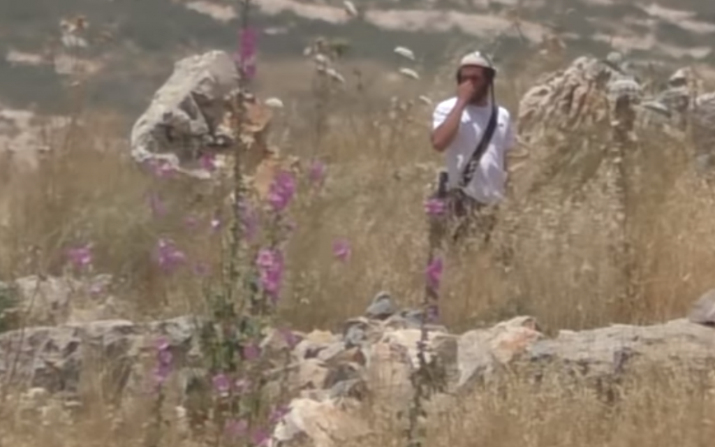 An off duty soldier stands in a Palestinian field in the northern West Bank moments before bending down and lighting brushes on fire. (Screen capture/YouTube)