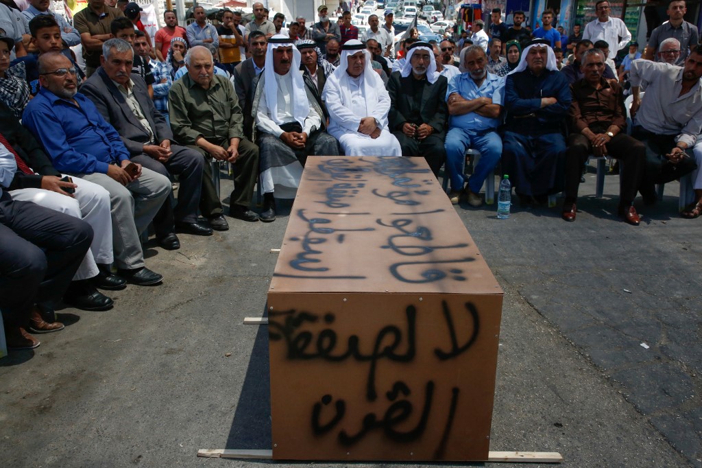 Palestinian men sit around a makeshift coffin with the words ‘No to the deal of the century,’ during a protest against a US-led meeting this week in Bahrain on the Palestinian-Israeli conflict, in the village of Yatta near the West Bank city of Hebron, on June 24, 2019 (HAZEM BADER / AFP)