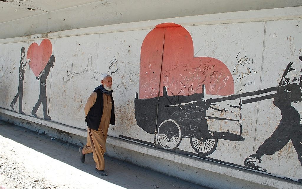 An Afghan man in Kabul passes a mural near the site of a deadly bombing, upon which are scrawled slogans reading, 'Death to Israel.' (Ezzatullah Mehrdad/ Times of Israel)