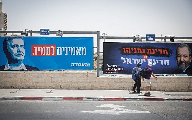 People walk near election campaign posters showing Labor party leader Amir Peretz, left, and Ehud Barak, right, at the entrance of Jerusalem on July 17, 2019. (Noam Revkin Fenton/Flash90)