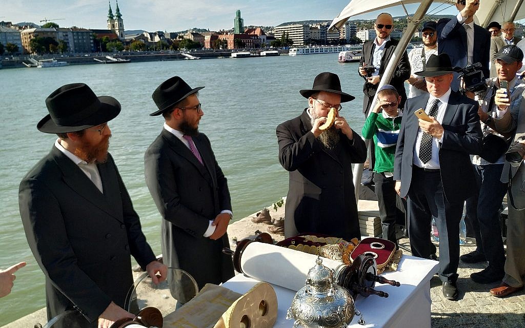 Rabbi Baruch Oberlander, right, blows the shofar horn on the bank of the Danube River at a ceremony dedicating two new synagogues and two new Torah scrolls in Budapest, September 22, 2019. (Yaakov Schwartz/ Times of Israel)