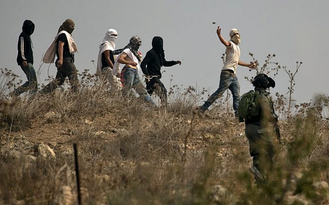 Illustrative: Israeli soldiers stand by as masked Israeli settlers throw stones at Palestinian protesters (unseen) gathering during a demonstration against construction on an Israeli outpost near the Palestinian village of Turmusaya and the settlement of Shilo, north of Ramallah in the West Bank, on October 17, 2019. (Jaafar Ashtiyeh/ AFP/ File)