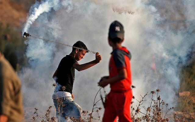 A Palestinian uses a slingshot to throw back a tear gas canister at Israeli forces during a riot along the border with Israel, east of Bureij in the central Gaza Strip, on October 18, 2019. (Mahmud Hams/AFP)