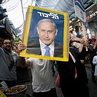 A Likud party supporter holds a campaign poster featuring then-prime minister Benjamin Netanyahu at Jerusalem's Mahane Yehuda market on April 7, 2019. (Yonatan Sindel/Flash90)