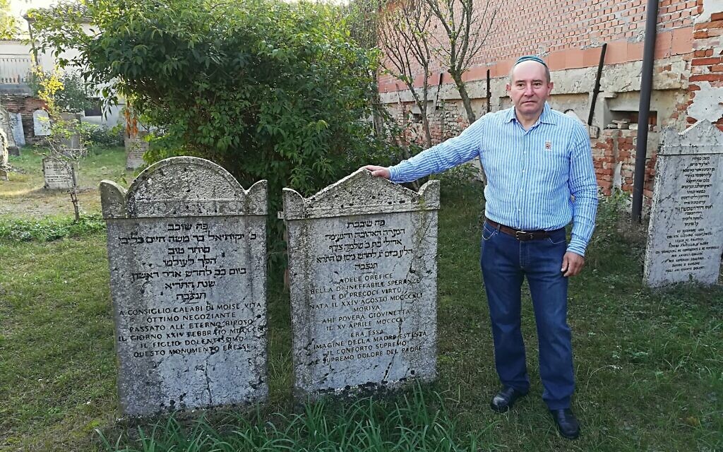 Giuseppe Minera next to two tombstones in the Jewish cemetery of Ostiano, Italy. (Giovanni Vigna/ Times of Israel)