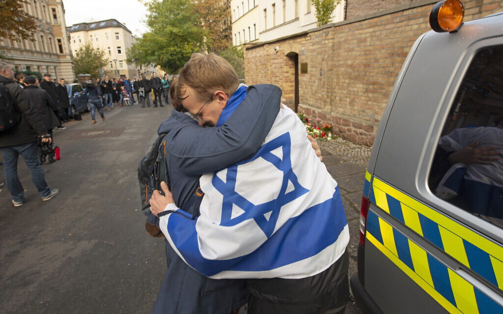 A person with a flag of Israel hugs another person in front of a synagogue in Halle, Germany, October 10, 2019. (AP Photo/Jens Meyer)