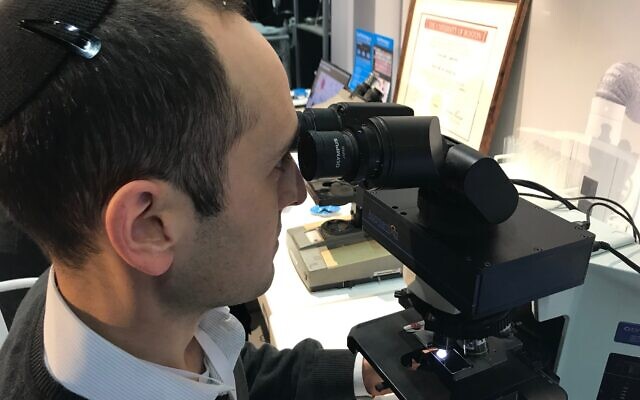 Augmentiqs has developed an electro-optic device that integrates within existing microscope and transforms them into smart and connected devices. Co-founder Gabe Siegel looking into the microscope at the HealthIL exhibit in Tel Aviv. November 27, 2019 (Shoshanna Solomon/Times of Israel)