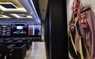 This picture from December 12, 2019, shows (L) a view of the exchange board at the stock market (Tadawul) in Riyadh displaying Aramco shares on the second day of their trading, along with a poster depicting Saudi Arabia's founder King Abdulaziz ibn Saud (C), his son and current King Salman bin Abdulaziz (R), and the latter's son Crown Prince Mohammed bin Salman. (Fayez Nureldine/AFP)