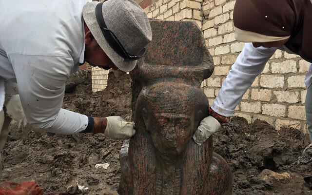 In this December 11, 2019, photo released by the Egyptian Ministry of Antiquities, archaeology workers clean a small pink granite statue of Ramses II, near the ancient pyramids of Giza, Egypt. (Egyptian Ministry of Antiquities via AP)