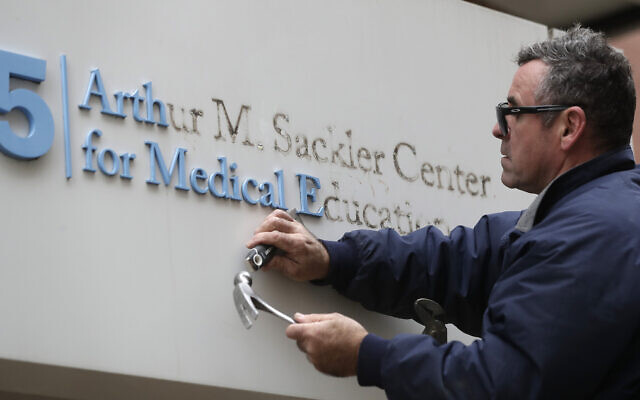 Worker Gabe Ryan removes a sign that includes the name Arthur M. Sackler at an entrance to Tufts School of Medicine, December 5, 2019, in Boston. (AP Photo/Steven Senne)