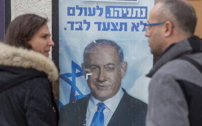 People look at a poster of Israel Prime Minister and governing Likud party leader Benjamin Netanyahu at a voting center in the northern Israeli city of Hadera, on December 26, 2019. (AP/Ariel Schalit)