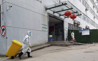 In this January 23, 2020, photo, a staff member wearing a hazardous materials suit hauls a bin at a hospital that reported a coronavirus death in Yichang in central China's Hubei Province.  (Chinatopix via AP)