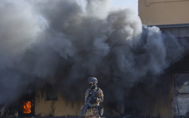 An Iraqi soldier stands guard in front of smoke rising from a fire set by pro-Iranian militiamen and their supporters in the US embassy compound , in Baghdad, Iraq, Wednesday, Jan. 1, 2020. (AP Photo/Nasser Nasser)
