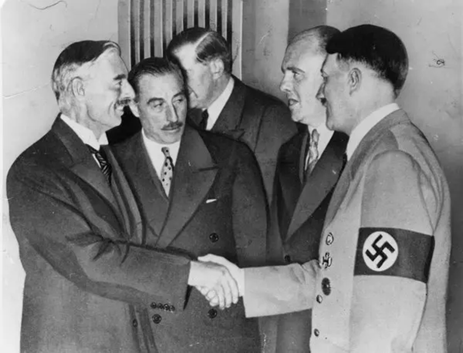 British prime minister Neville Chamberlain, left, shakes hands with Hitler to seal the Munich Agreement. (Public domain)