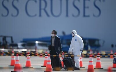 A passenger (L) disembarks from the Diamond Princess cruise ship – in quarantine due to fears of the new COVID-19 coronavirus – at the Daikoku Pier Cruise Terminal in Yokohama on February 19, 2020. (Photo by CHARLY TRIBALLEAU / AFP)