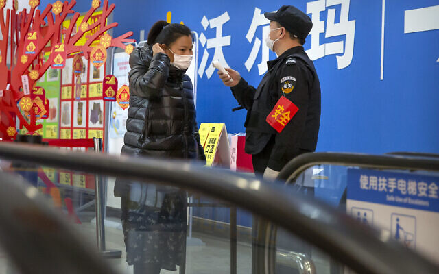 A security guard takes a customer's temperature at the entrance to a grocery store in Beijing, February 1, 2020. (AP Photo/Mark Schiefelbein)