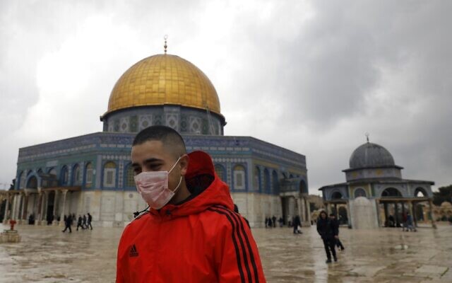 A young man wearing a protective mask as a measure of protection against the coronavirus COVID-19, walks in front of the Dome of the Rock shrine inside the al-Aqsa compound on the Temple Mount in the Old City of Jerusalem, March 13, 2020. (Ahmad GHARABLI/AFP)