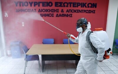 A worker wearing a protective suit sprays disinfectant inside a citizen's service office in the Athens' eastern suburb of Dafni, March 9, 2020. The sign reads "Interior Ministry. Municipality of Dafni." (Thanassis Stavrakis/AP)